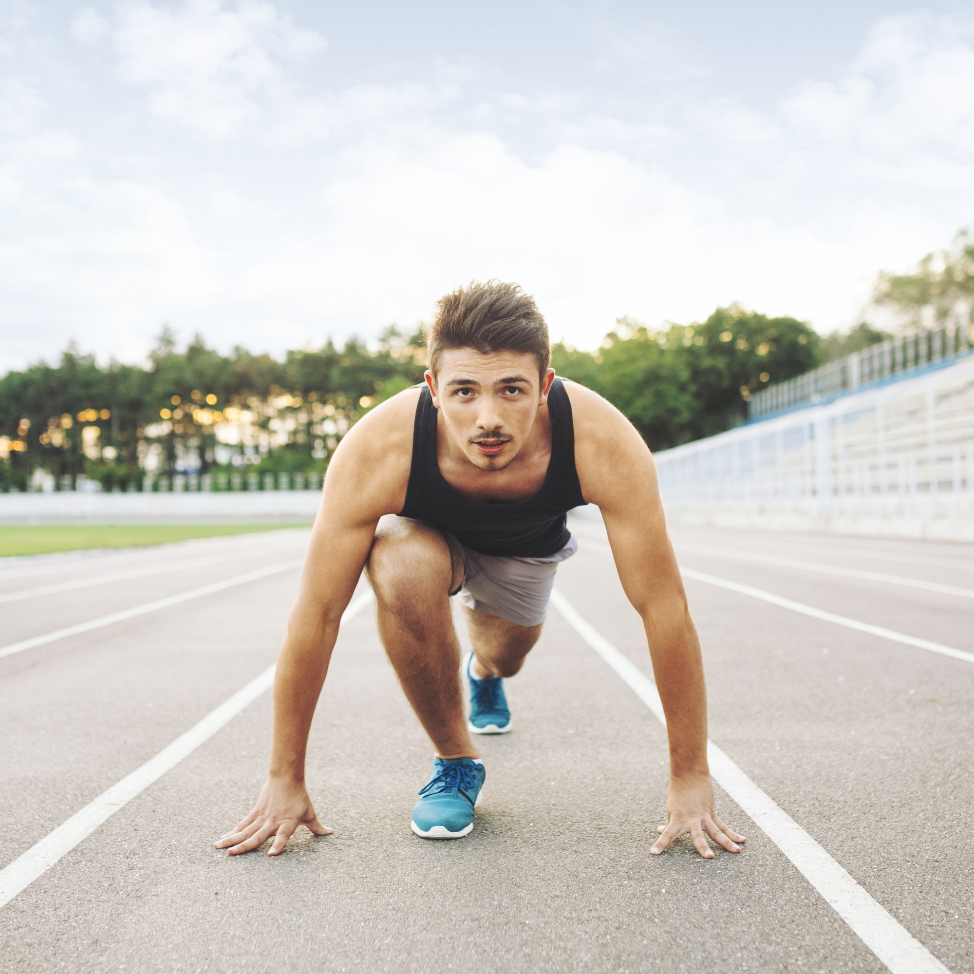 homem com camiseta regata preta em pista de corrida, posicionado para iniciar a correr.